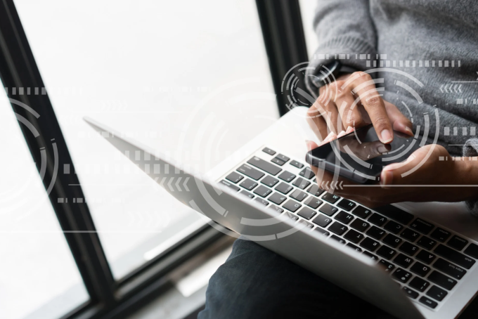 cybersecurity portrayed by man on multiple connected devices using info transfer.